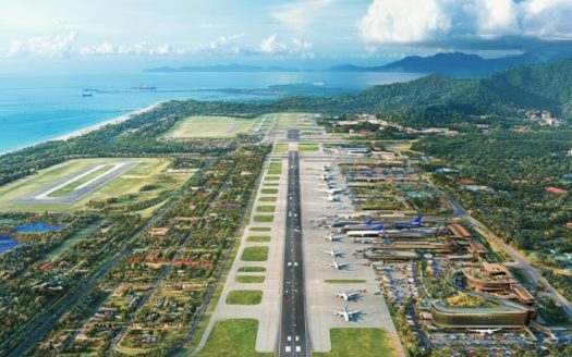 Aircraft runway at an airport with surrounding greenery and ocean view.