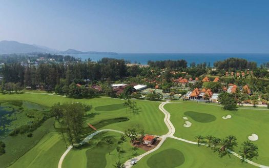 Golf course with ocean view and lush greenery in the background.