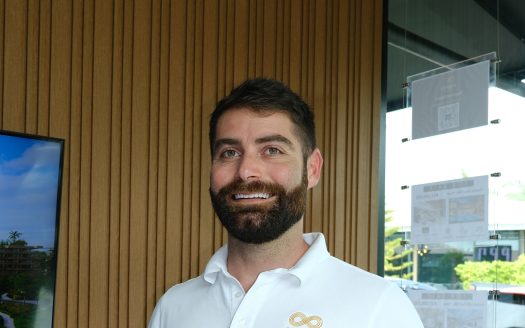 Marcus Divirgilio at Anan Property Group, smiling in office with wooden wall background.