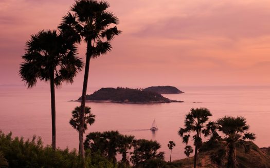Sunset over tropical coastline with palm trees and calm sea, showcasing serene island views.
