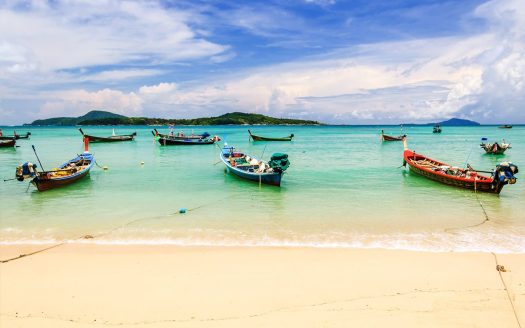 Beach scene with colourful boats anchored in clear turquoise waters.