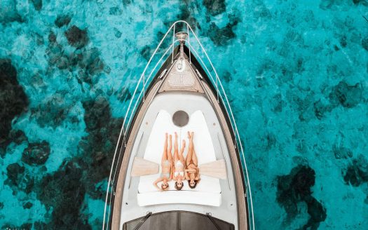 Luxury yacht sailing in turquoise sea with two women relaxing on deck.