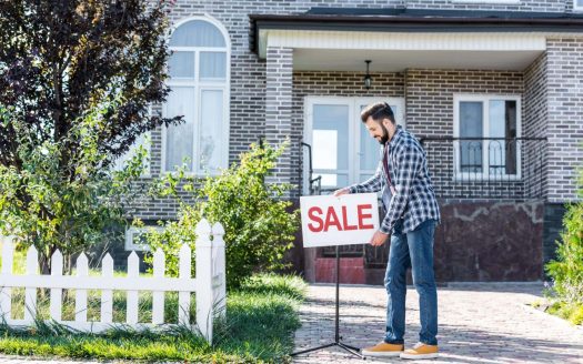 Man placing sale sign outside brick house