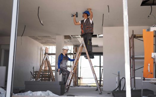 Construction workers installing ceiling wiring on ladders