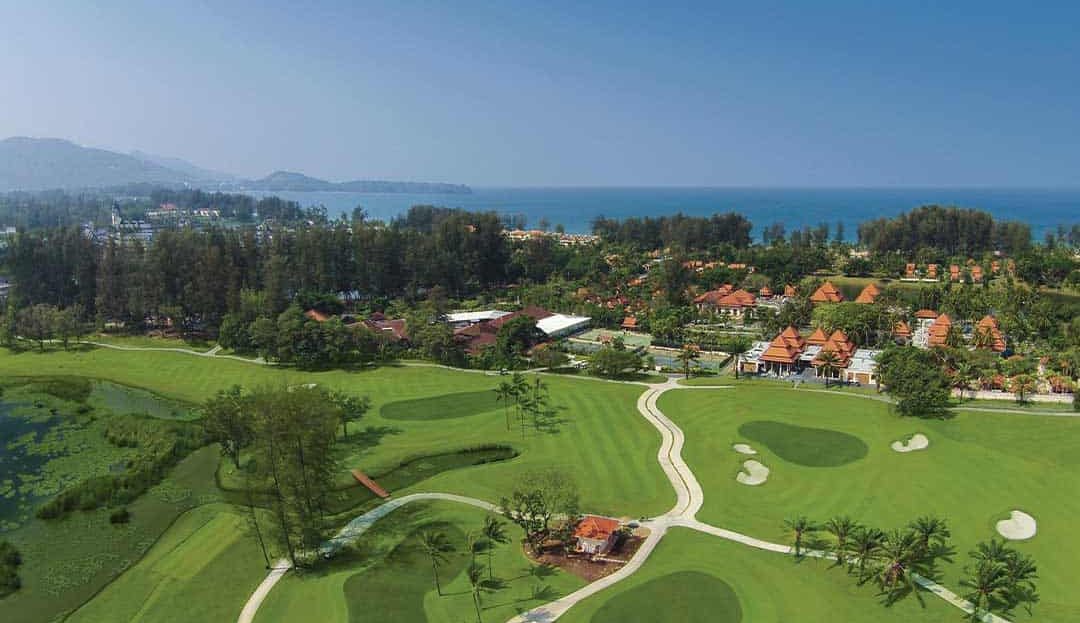 Golf course with ocean view and lush greenery in the background.