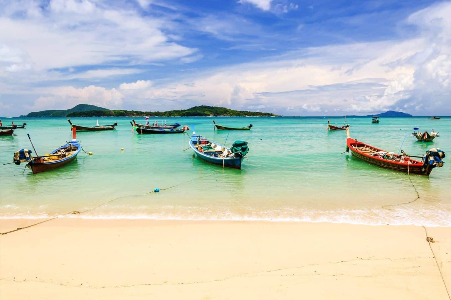 Beach scene with colourful boats anchored in clear turquoise waters.