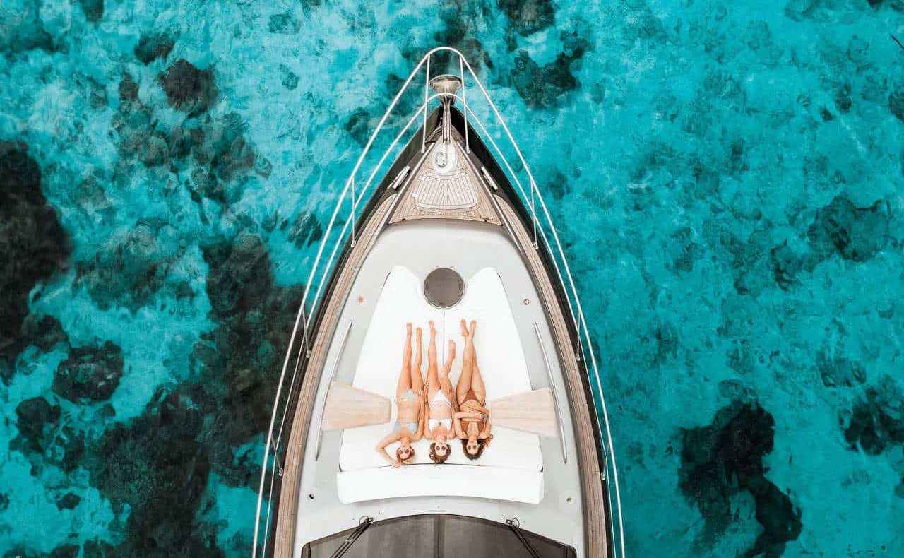 Luxury yacht sailing in turquoise sea with two women relaxing on deck.