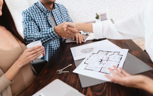 Couple shaking hands with estate agent over house plans