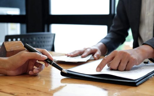 Person signing contract while adviser points at document