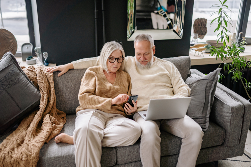 Older couple using smartphone and laptop on sofa